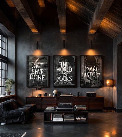History in the Making Collection room mockup: three monochrome classical architecture artworks with GET SHIT DONE, THE WORLD IS YOURS and MAKE HISTORY lettering, shown above a cabinet in a dark living room.