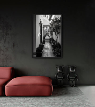 Poverty in Richness room mockup: a monochrome bright passage lined with plants and steps, shown above a red chaise.